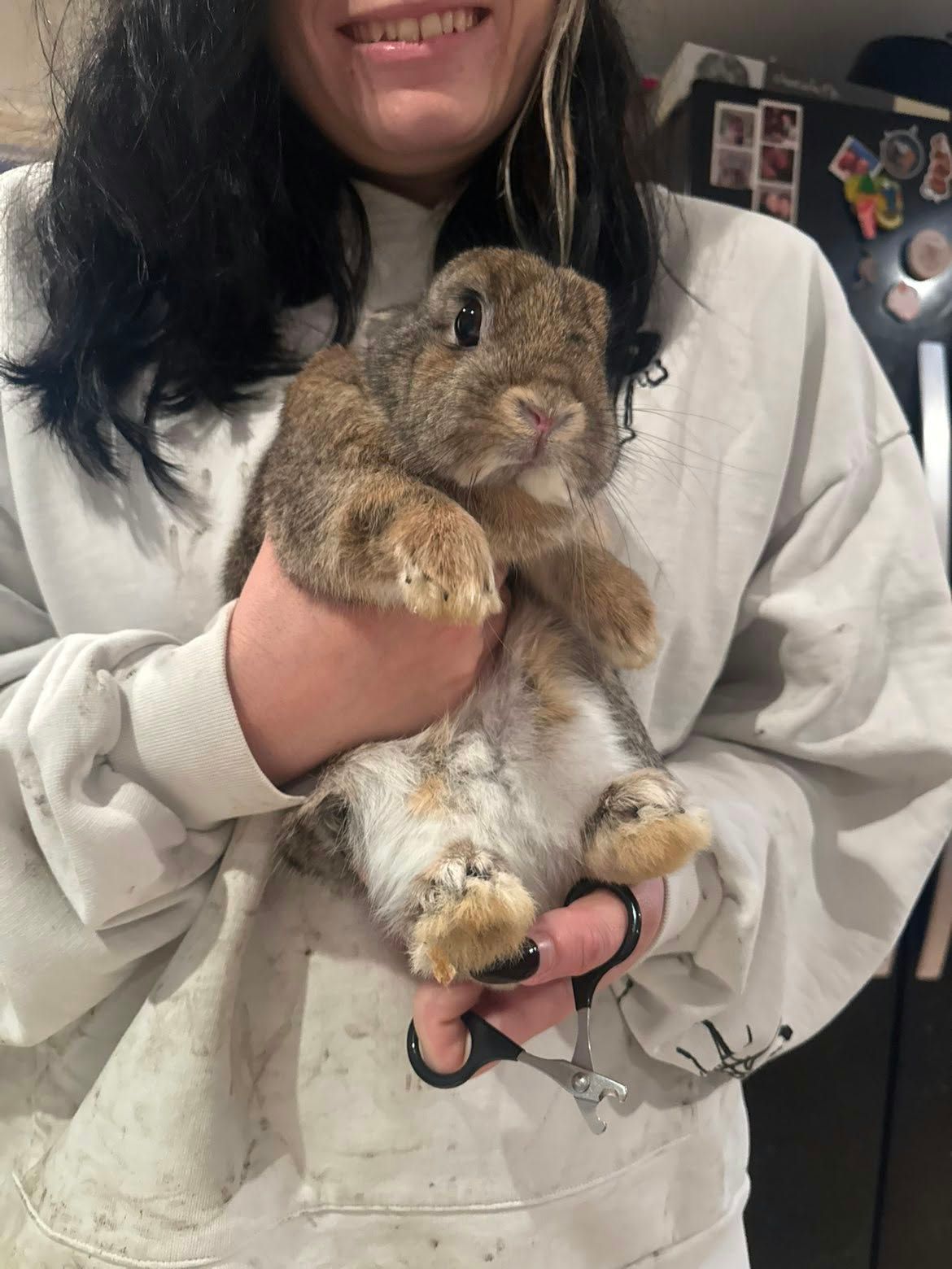 Jenny smiling while holding a wide-eyed brown rabbit, with small nail clippers in her hand
